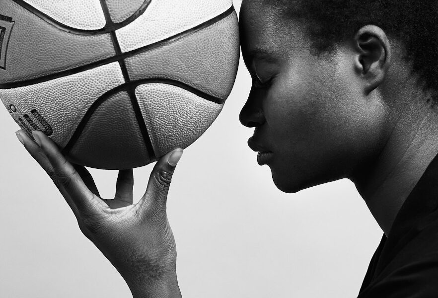 Profil Bild Frau, die Basketball in der gespreizten linken Halt hält. Ball berührt die Stirn der Frau