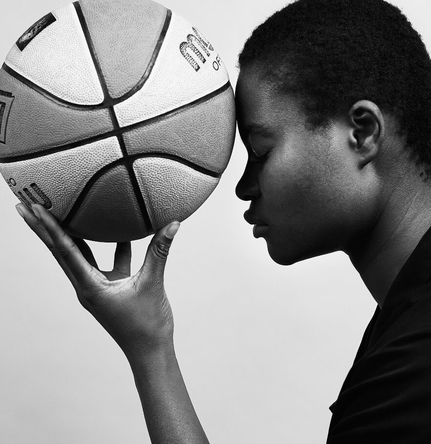 Profil Bild Frau, die Basketball in der gespreizten linken Halt hält. Ball berührt die Stirn der Frau