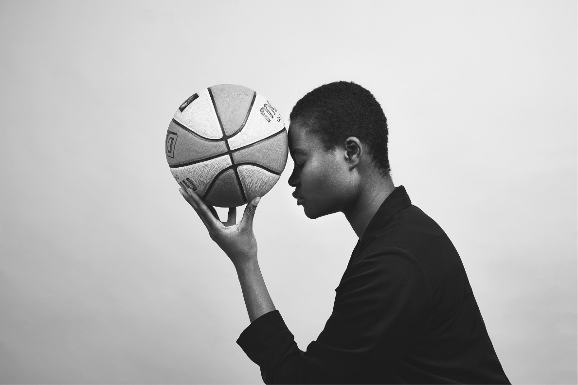 Frau seitlich mit Basketball in linker Hand und Kopf berührt Ball